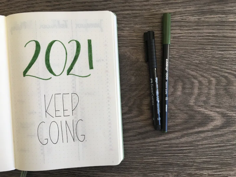 Bullet-Journal-Deckblatt mit grünem Schriftzug 2021 Keep Going neben zwei Stiften