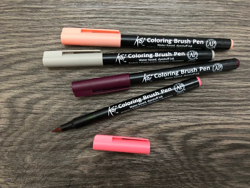 Vier Koi Coloring Brush Pens in Apricot, Beige, Beere und Pink auf Holzuntergrund