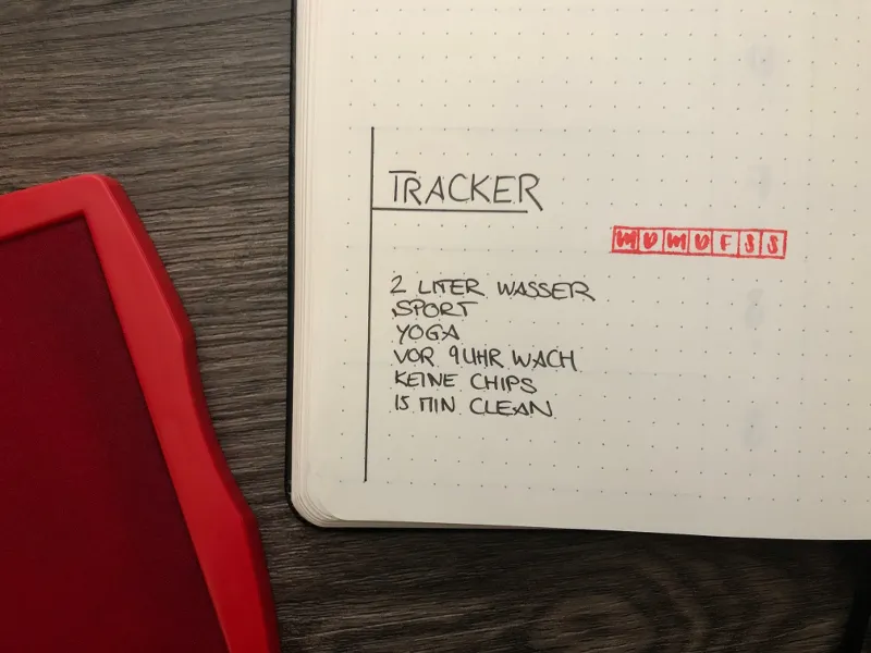 Bullet-Journal-Tracker mit gestempelten Wochentagskürzeln und einer Liste von Gewohnheiten, daneben ein rotes Stempelkissen
