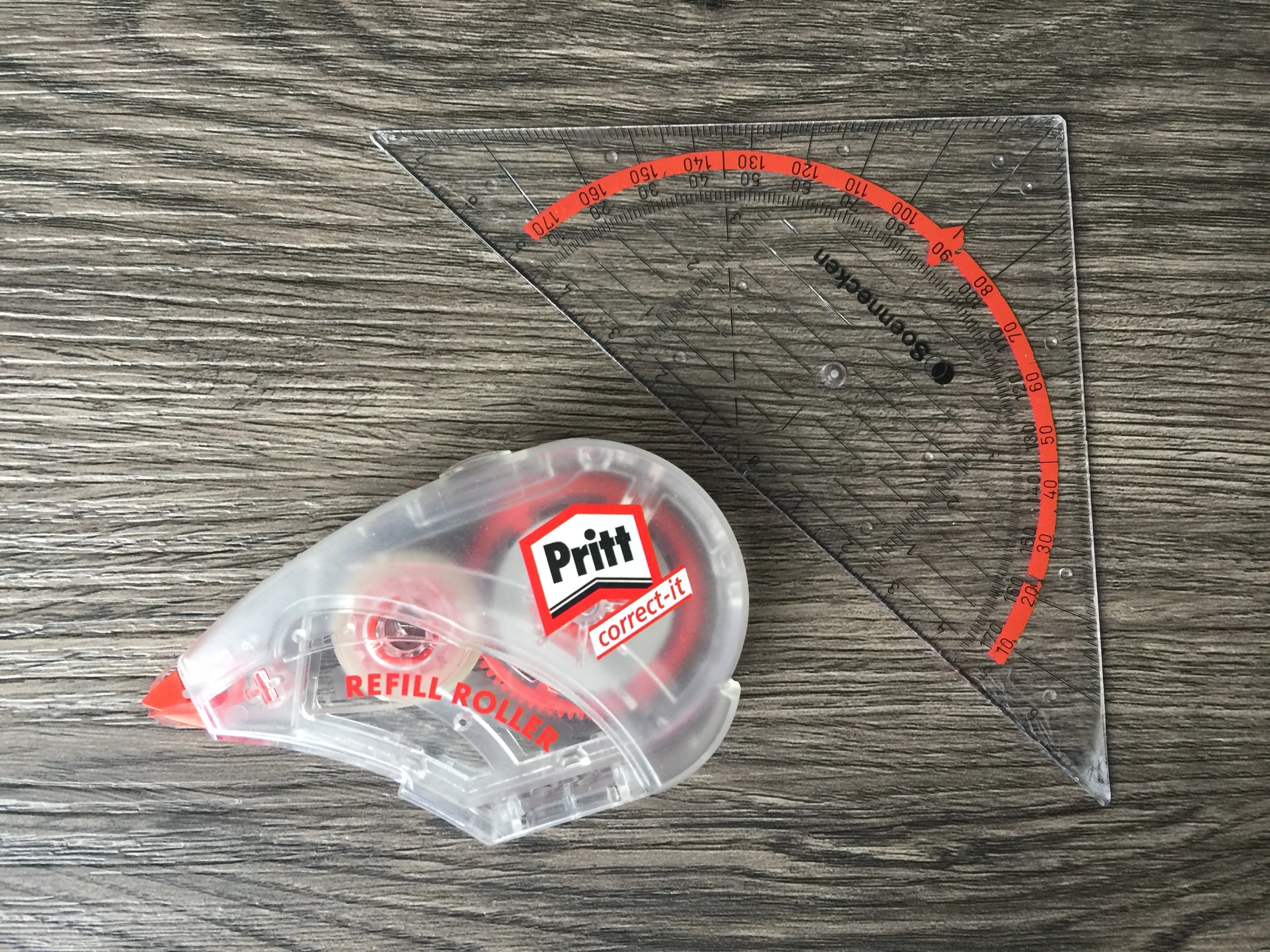 Transparentes Geodreieck und ein Pritt Korrekturroller auf Holz