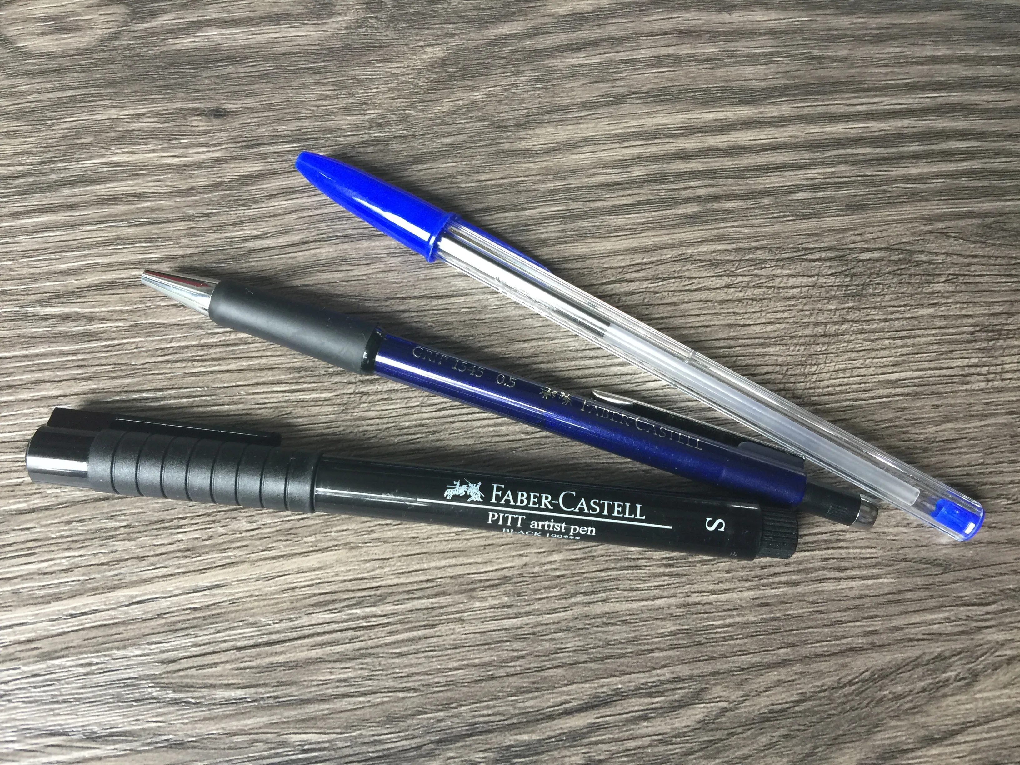 Kugelschreiber, Faber-Castell Druckbleistift und PITT Fineliner auf Holztisch