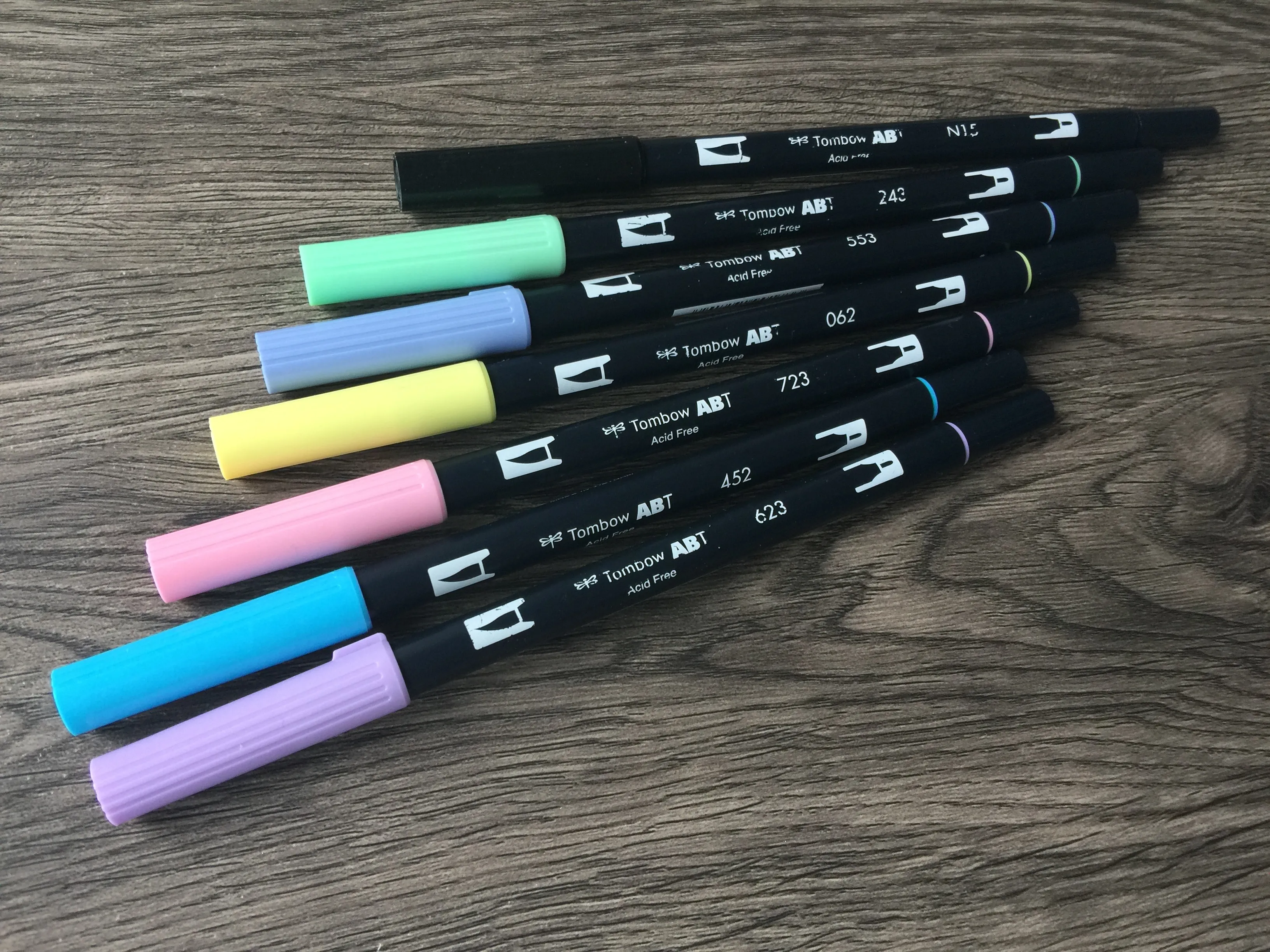 Acht Tombow ABT Brushpens in Pastellfarben aufgefächert auf Holz