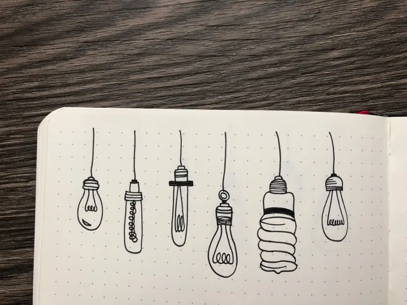 Reihe gezeichneter haengender Gluehbirnen als Doodles auf Notizbuchseite