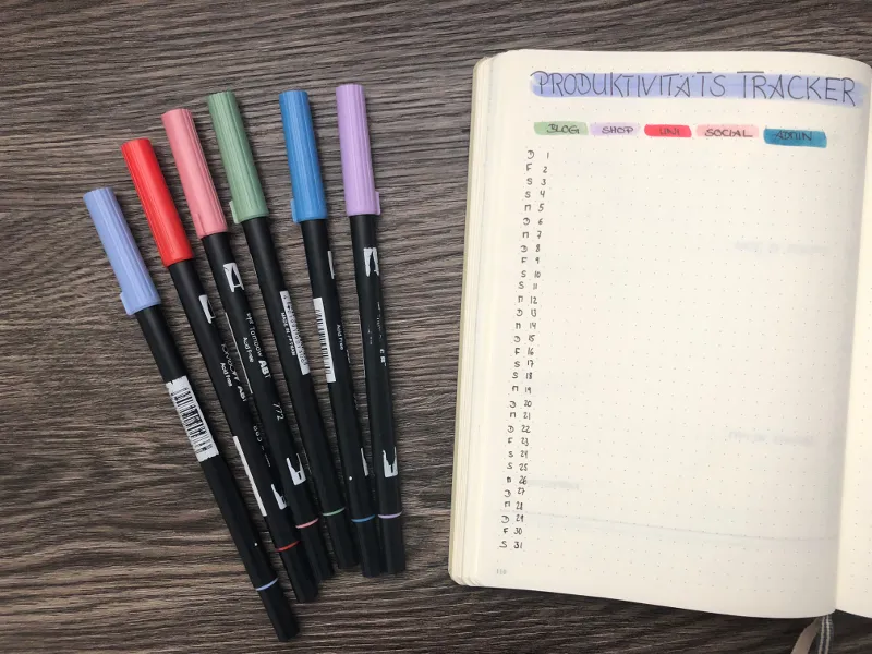 Produktivitäts-Tracker neben bunten Brushpens auf dem Holztisch