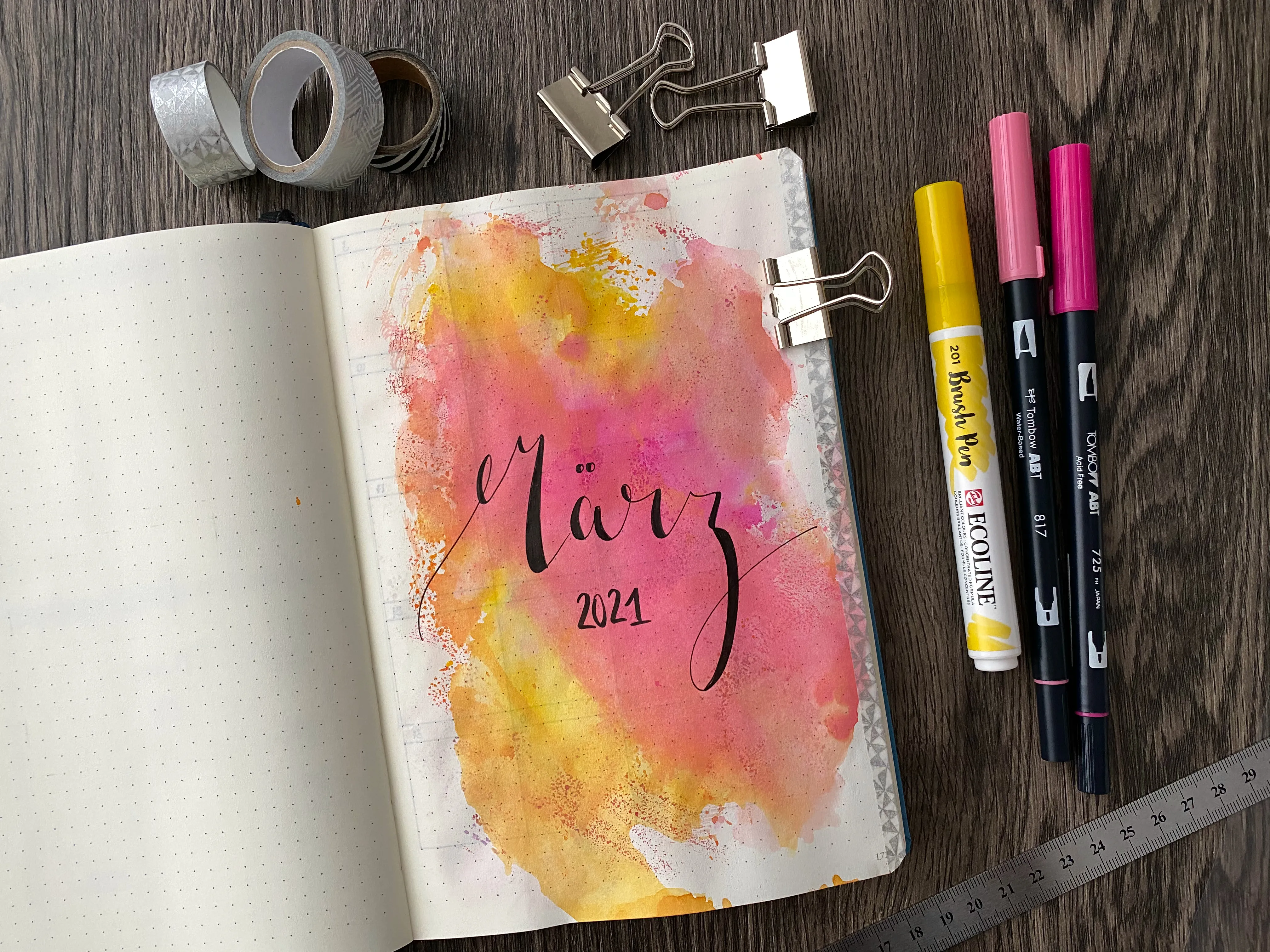 Bullet-Journal-Deckblatt März 2021 mit orange-pinkem Aquarellklecks, Brush Pens und Washi Tape