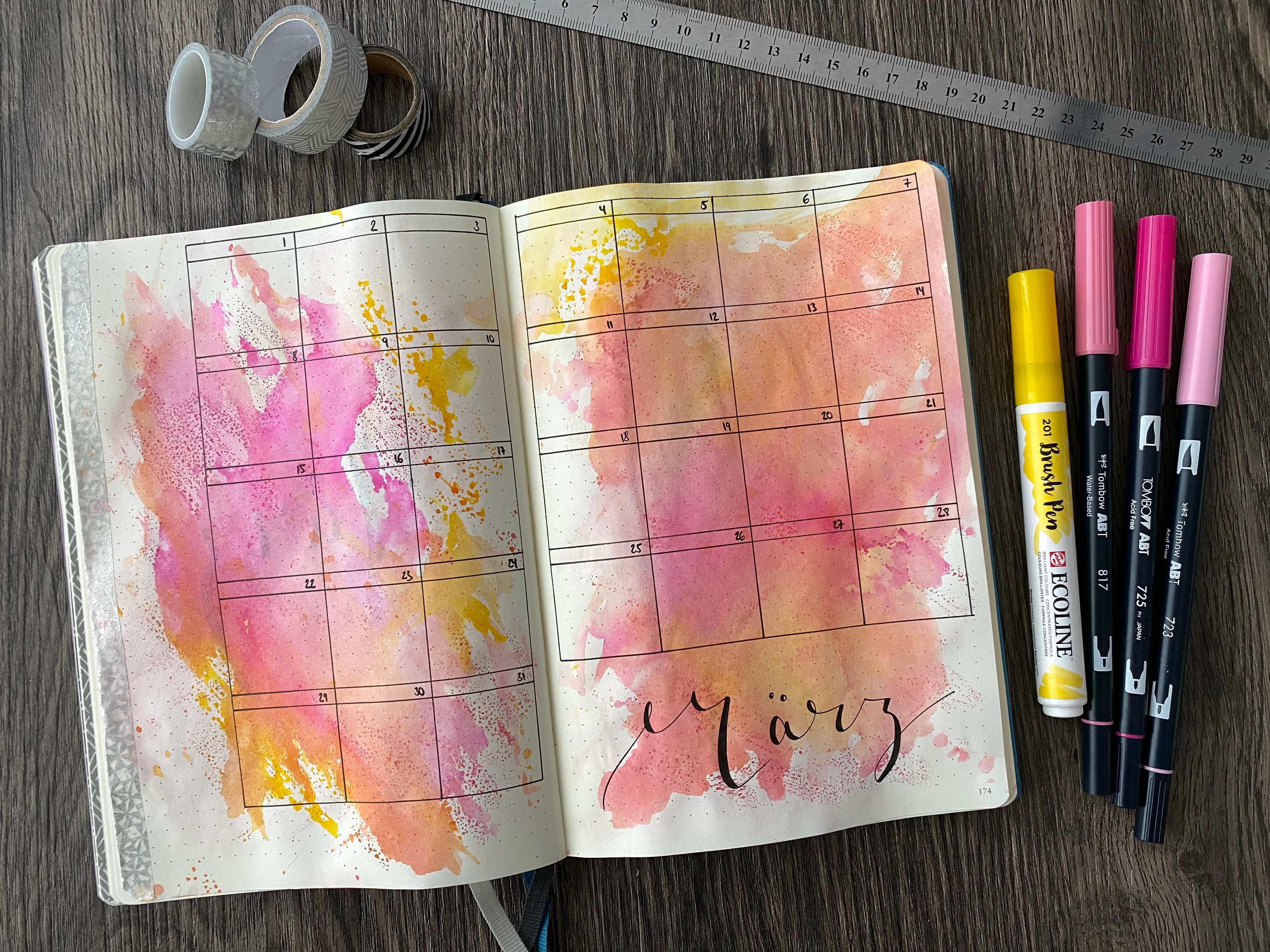 Monatsübersicht März als Kalenderraster über zwei Seiten mit rosa-gelbem Aquarell-Hintergrund, daneben Brush Pens und Washi Tape