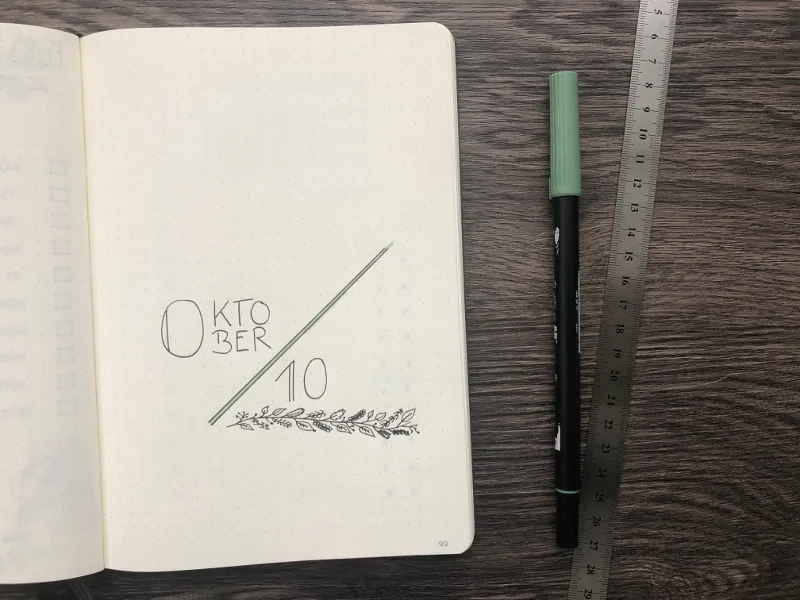 Minimalistisches Monatsdeckblatt Oktober mit filigranem Blätterzweig, daneben ein grüner Brushpen und ein Lineal
