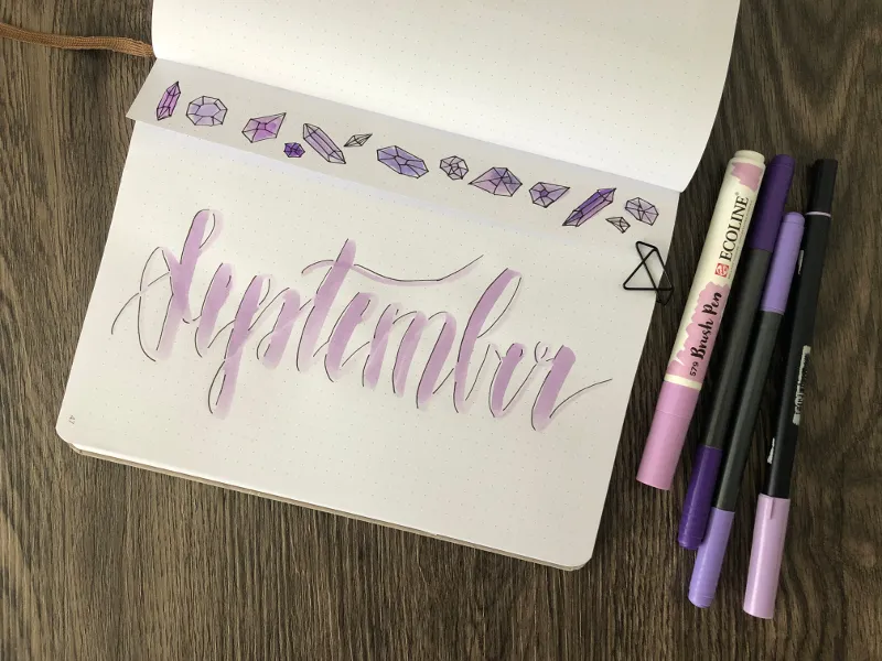 September-Deckblatt in Lila mit gezeichneten Kristallen und Ecoline Brush Pens