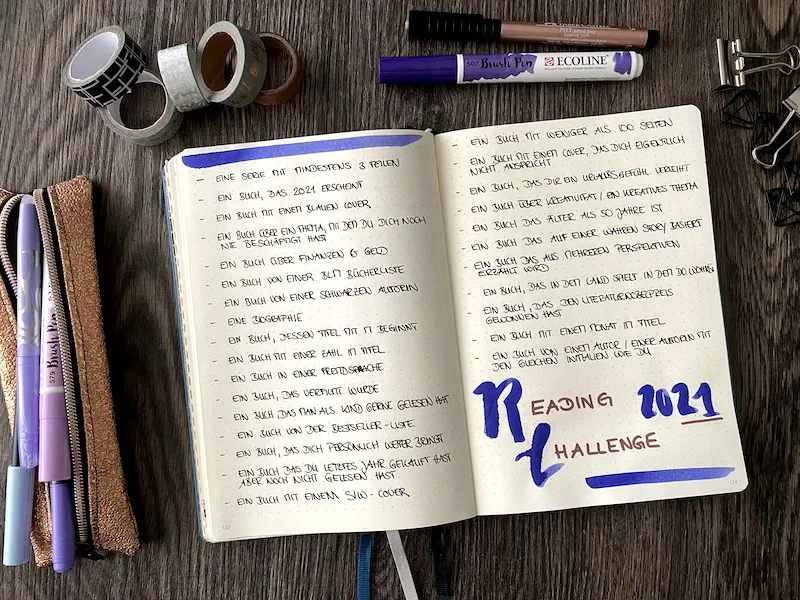 Aufgeschlagenes Bullet Journal mit der handgeschriebenen Reading Challenge 2021 und einer Liste von Buchkategorien, umgeben von Washi-Tape und Brushpens