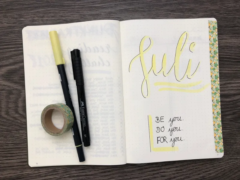 Aufgeschlagenes Bullet Journal mit Juli-Handlettering, Stiften und Washi-Tape