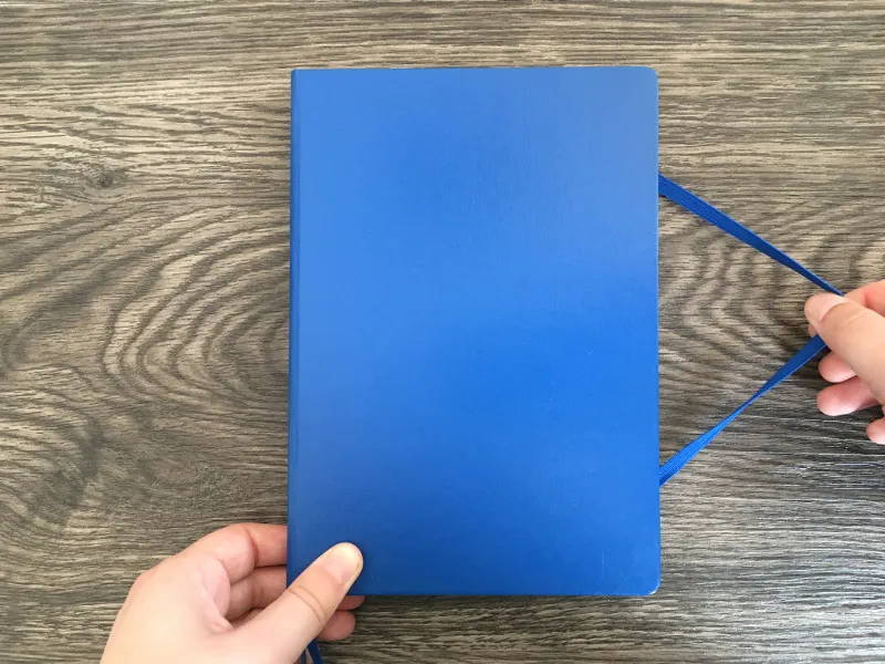 Blaues Notizbuch, Hände spannen das Gummiband über die Rückseite