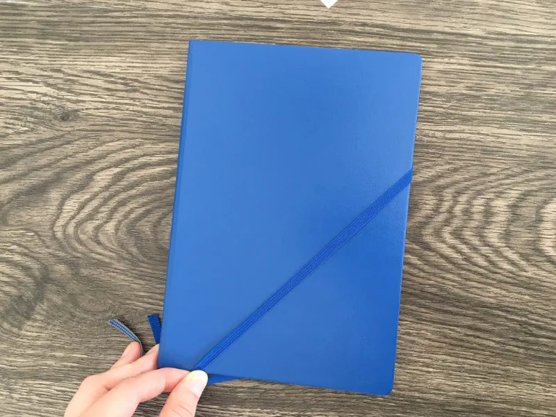 Blaues Notizbuch mit diagonal über die Rückseite gelegtem Gummiband