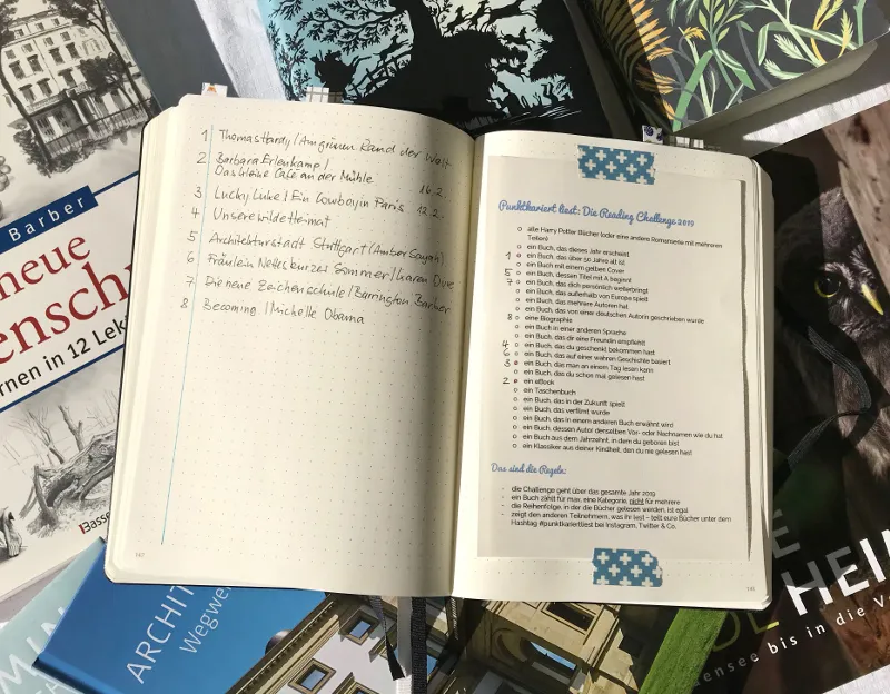 Aufgeschlagene Bücherliste zur Reading Challenge 2019 zwischen Büchern
