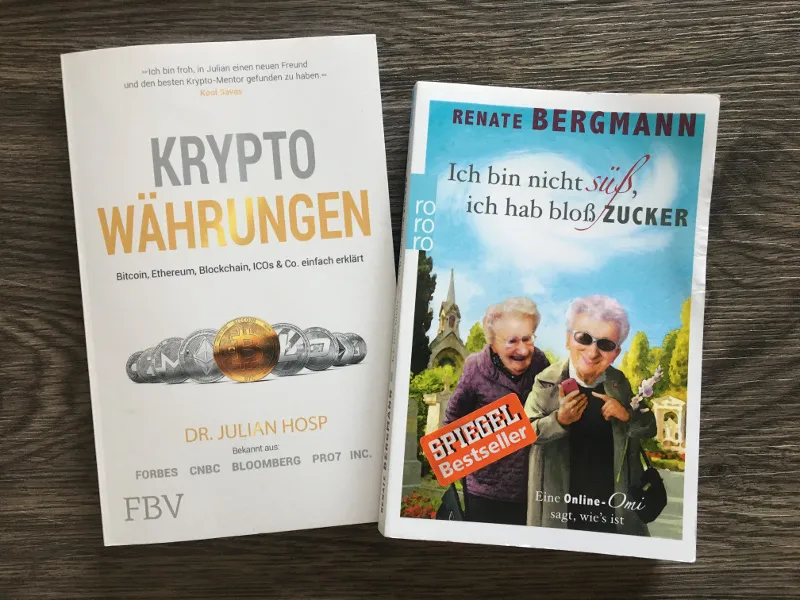 Zwei Taschenbücher Kryptowährungen und ein Renate-Bergmann-Roman auf Holzuntergrund