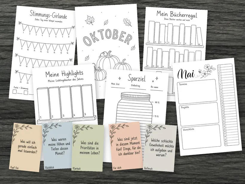 Vorlagen aus allen 4 Sets auf dunklem Holz ausgelegt: Stimmungs-Girlande und Sparziel aus dem Tracker-Set, Bücherregal und Highlights aus dem Bücher-Set, das Oktober-Deckblatt und die Mai-Übersicht aus dem Monats-Set und vorne 5 farbige Fragekarten.