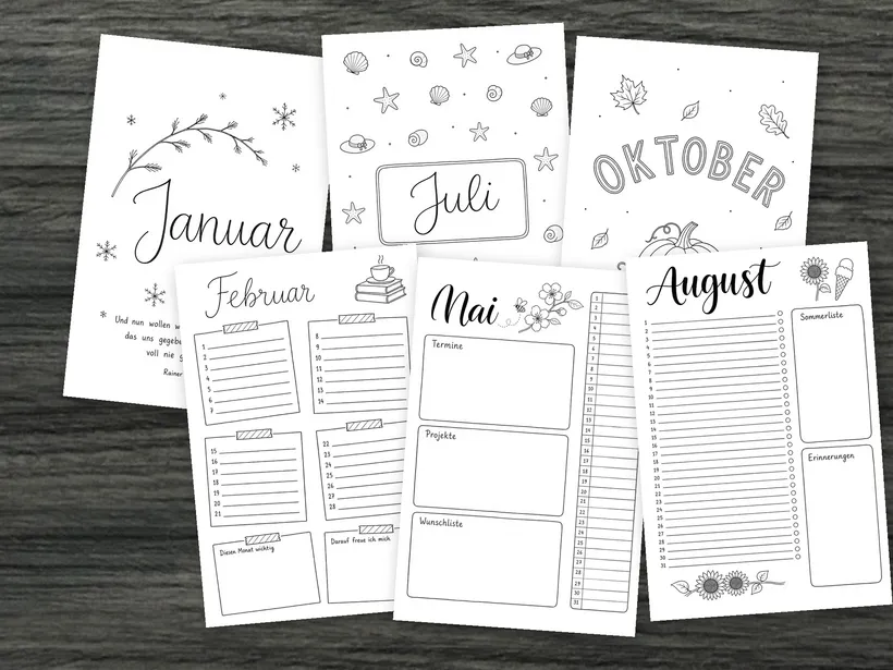 Sechs Blätter des Monats-Sets, leicht gedreht und überlappend auf dunklem Holz ausgelegt: die Deckblätter Januar, Juli und Oktober und die Monatsübersichten Februar, Mai und August.